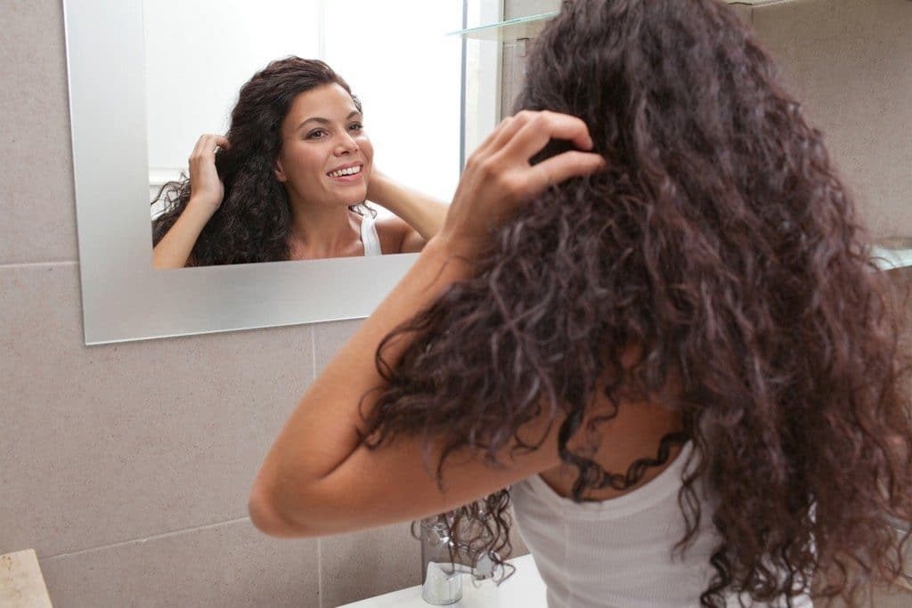 Mulher de cabelo cacheado se olhando no espelho